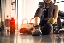 Close Up Of Woman Using Smart Phone And Holding Apple While Workout In Fitness Gym. Sport And Technology Concept. Lifestyles And Healthcare Theme.