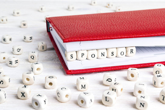 Word Sponsor written in wooden blocks in red notebook on white wooden table.
