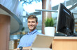 © ty - Portrait of happy man sitting at office desk, looking at camera, smiling.