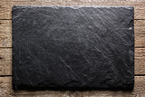 Fototapeta Desenie - Black slate board on grunge wooden table closeup. Natural texture. Can be used like food background