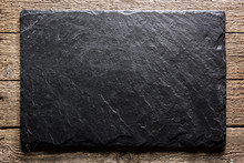 Black Slate Board On Grunge Wooden Table Closeup. Natural Texture. Can Be Used Like Food Background
