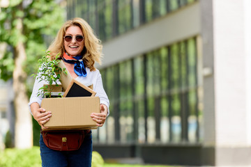 Wall Mural - smiling attractive woman holding paper box with office stuff on street