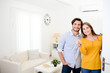 © W PRODUCTION - cheerful young couple man and woman welcome friends at open front door new student home apartment