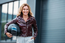 Smiling Woman In Leather Jacket Holding Motorcycle Helmet On Street And Looking Away