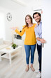 © W PRODUCTION - cheerful young couple man and woman welcome friends at open front door new student home apartment