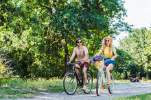 Young Happy Couple Riding Retro Bicycles In Park On Summer Day