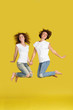 © Rithor - Full height shot of two caucasian dressed equally in jeans and white t-shirts jumping for joy, happy with coming holidays over yellow background studio. Best friendship and family