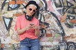 Frau mit Kopfhöhrer und Handy an Graffitiwand