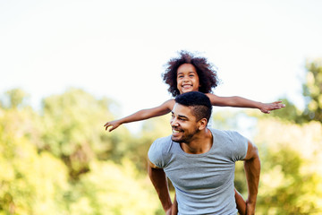 portrait of young father carrying his daughter on his back