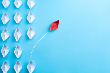 group of white paper ship in one direction and one red paper ship pointing in different way on blue 