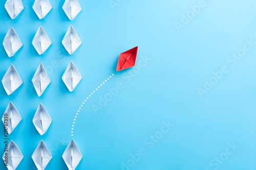 Fotomural Group of white paper ship in one direction and one red paper ship pointing in different way on blue background
