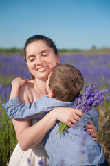 happy smiling mother kissed by her child with love among lavender meadow