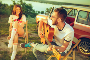 Couple sitting and resting on the beach playing guitar on a summer day near river