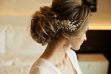 Wedding hairstyle of beautiful and fashionable brown-haired model girl in a lace dress, with earrings and jewelry in her hair