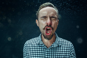 Young handsome man with beard sneezing, studio portrait