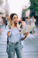 Wall Mural - Young beautiful female traveler lost in the city using map and mobile phone 