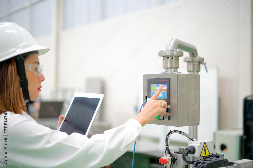 Factory worker is programming a CNC milling machine with a tablet computer.