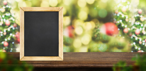 Poster - blackboard on dark brown wood table top with abstract blur christmas tree red decor ball and snow fall background with bokeh light,winter Holiday banner,Mock up for display of product.