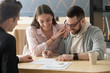 Excited millennial couple signing purchase agreement buying first home together, husband puts signature on document, becoming apartment owner, spouses legalize property ownership in realtor office
