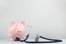 Pink Piggy Bank With Stethoscope And Coins On Grey Background