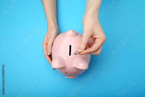 Fotomural Female hand putting coin into piggy bank on blue background