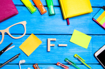 A wooden letter of grade F minus the student's desk. School supplies on a blue wooden table. The concept of higher school assessment, poor performance, a shameful sign. Bad student.