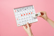 Close up female holds in hand thermometer, female periods calendar for checking menstruation days isolated on trending pink background. Medical healthcare, ovulation gynecological concept. Copy space.