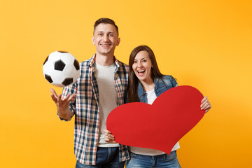 Wall Mural - Young happy cheerful couple supporter, woman man, football fans cheer up support team, holding red heart love, soccer ball isolated on yellow background. Sport family leisure people lifestyle concept