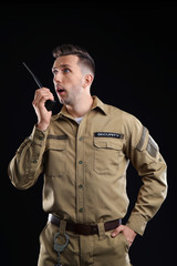 Wall Mural - Male security guard using portable radio transmitter on dark background