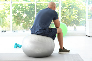 Sticker - Tired overweight man sitting on fitness ball in gym