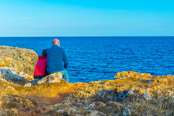 an old couple is enjoying sunset on coastline of mallorca