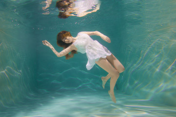 Underwater scene. Girl mermaid with healthy shiny beautiful long hair. A woman, a fashion model in the water in a beautiful dress swims like a fish.