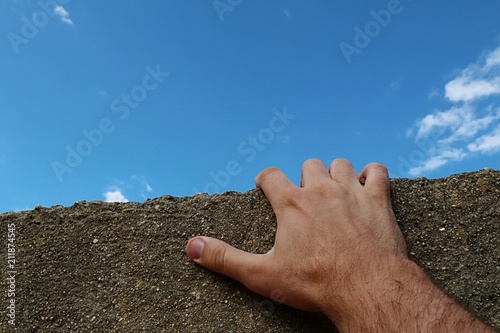 Fotografía Adult male man hand holding edge of small concrete shed roof, trying to climb on it