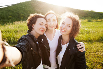 Beautiful and happy positive mom and grown-up daughters are walking around nature and making a selfie on a smartphone