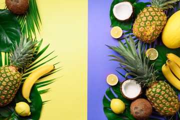  Exotic pineapples, coconuts, banana, melon, lemon, tropical palm and green monstera leaves on yellow, violet background with copyspace. Creative layout. Monochrome summer concept. Flat lay, top view.