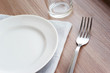 © Elena - Empty white plate on a gray napkin with fork and glass on brown table. Table setting, preparation for meals.