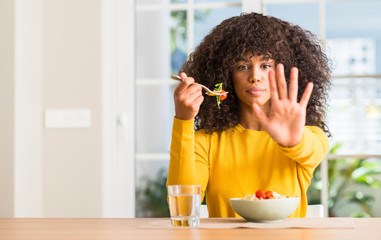 Poster - African american woman eating pasta salad at home with open hand doing stop sign with serious and confident expression, defense gesture