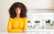 © Krakenimages.com - African american woman wearing yellow sweater at kitchen with serious expression on face. Simple and natural looking at the camera.