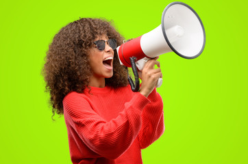 african american woman wearing sunglasses communicates shouting loud holding a megaphone, expressing