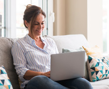 Middle Aged Woman Using Laptop In The Sofa With A Happy Face Standing And Smiling With A Confident Smile Showing Teeth
