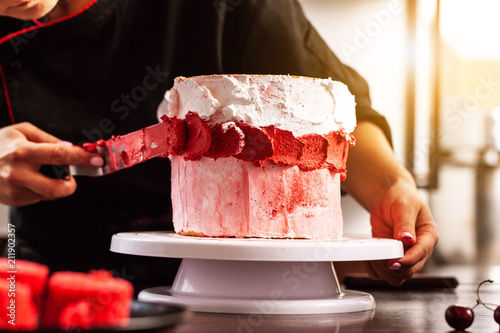 Zdjęcie XXL dziewczyna szefa kuchni cukiernik podejmowania ciasto oleju z wiśni. koncepcja procesu produkcji w domu ciasta do zamawiania klientów. rozmazuje szpachelkę do kremów. zdjęcie w tle.