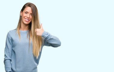 Poster - Beautiful young woman wearing sweater and jeans happy with big smile doing ok sign, thumb up with fingers, excellent sign