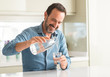 © Krakenimages.com - Middle age man drinking a glass of water with a happy face standing and smiling with a confident smile showing teeth