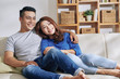 © DragonImages - Handsome Asian man and pretty woman cuddling on couch at home and looking dreamily away in daylight
