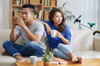 Asian couple sitting on couch and man surfing smartphone while woman looking bored and lonely