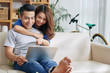 © DragonImages - Beautiful Asian young couple on sofa at home surfing laptop together and smiling happily