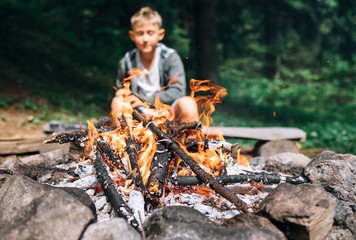 boy sits near campfire. summer camping time