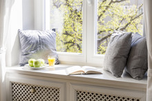 Grey Cushions, Book, Apples And Orange Juice On Window Sill In White Interior. Real Photo