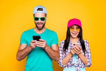 Electronic wireless device sms media cellular concept. Portrait of joyful cheerful couple using smart phones typing message browsing 3G wifi internet isolated on vivid yellow background
