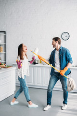 couple in rubber gloves having fun with mop and pretending singing in kitchen